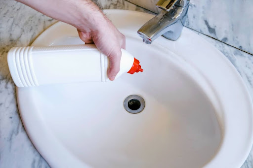 Homeowner using chemical drain cleaner to clear bathroom sink drain.